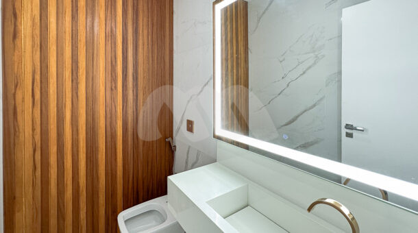 Lavabo da casa com espelho iluminado, pia branca e painel de madeira, à venda na barra da tijuca