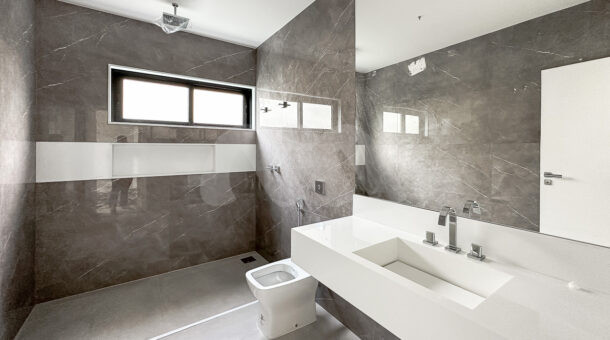 Banheiro do home cinza com um chuveiro, espelho e pia branca, à venda no alphaville