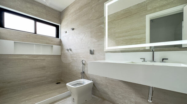 banheiro da terceira suíte, com piso e parede cor bege e um chuveiro, à venda na barra da tijuca