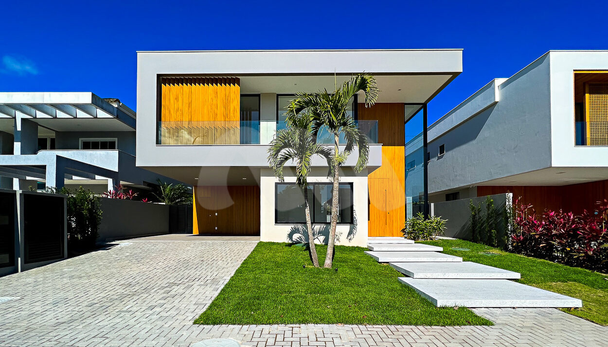Fachada da casa contemporânea de luxo cinza com detalhes de madeira, com gramado e bonito paisagismo, à venda na Barra da Tijuca