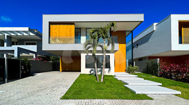 Fachada da casa contemporânea de luxo cinza com detalhes de madeira, com gramado e bonito paisagismo, à venda na Barra da Tijuca