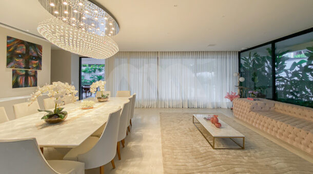 Sala de jantar integrada com sala de estar, com ampla mesa de jantar branca e lustre em cristais