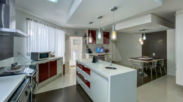cozinha com grande bancada, lustres e armário brancos e vermelhos