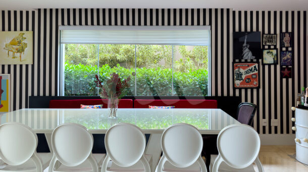 Sala de jantar com banco, mesa branca e cadeiras brancas, parede em listras preto e branco