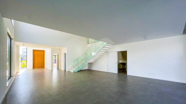 Sala com piso cinza escuro e parede branca com escadas com proteção de vidro, à venda no alphaville