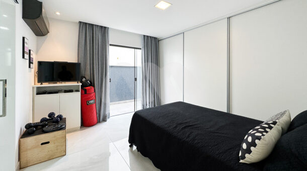 Imagem lateral do quarto com cama de solteiro da mansão moderna à venda na Muller Imóveis RJ.