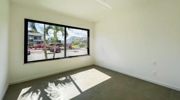 Suite térrea com paredes brancas e piso cinza escuro, janela coma vista externa, à venda na barra da tijuca