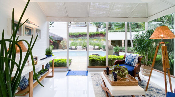 Sala de leitura com poltronas, paredes em vidro com vista para jardim, decoração em tons de azul, branco e madeira
