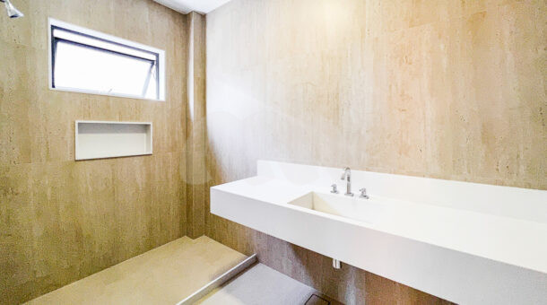 Banheiro da suíte com chuveiro, parede de porcelanato marrom claro e pia de mármore branco, à venda na barra da tijuca