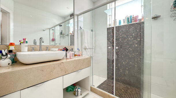 Banheiro com box em ladrilhos marrom, bancada com cuba e armário planejado