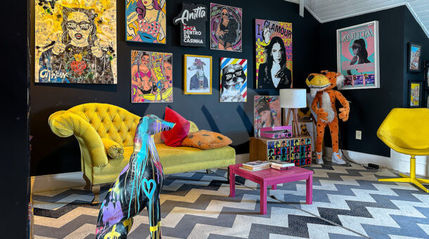 área de estúdio com sofá amarelo, tapete listrado, parede em quadros e decoração moderna