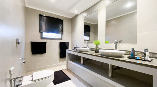 Banheiro com bancada com cubas duplas, armário planejado e iluminação em teto planejada