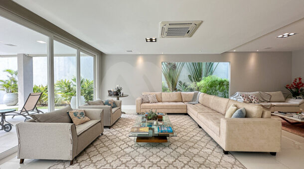 Imagem de sala de estar com sofá de canto, poltronas e tapete em casa triplex de alto padrão na Barra da Tijuca