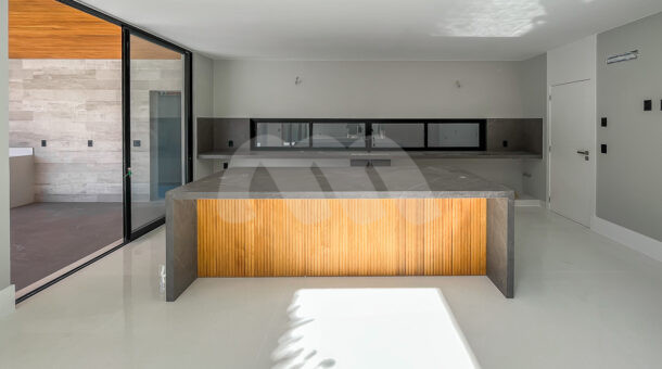 Imagem de cozinha interna com ilha em pedra cinza e ripas de madeiras, e bancada ao fundo da casa contemporanea lindissima a venda
