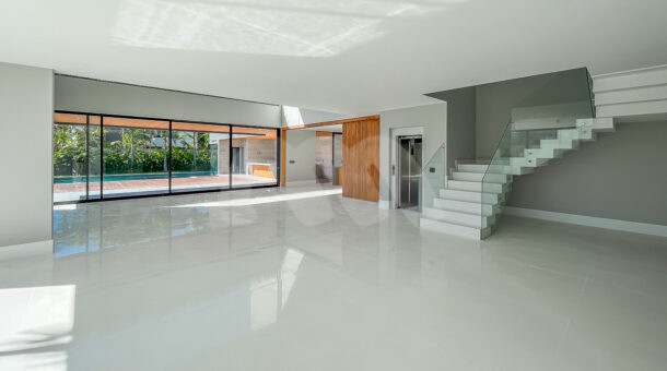 Imagem de ampla sala em vários ambientes, com porcelanato branco brilhante e escada brancada em 3 niveis da casa a venda na barra da tijuca