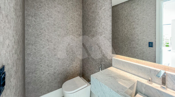 Imagem de lavabo com parede em cimento queimado, bancada de pedra branca com pia esculpida e vaso