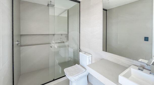 Imagem de banheiro com bancada branca, cuba, vaso e box até o teto com chuveiro
