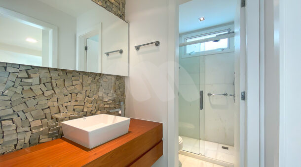Imagem lateral do banheiro com vista da pia da mansão moderna à venda na Muller Imóveis RJ.
