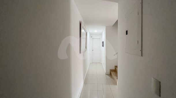 Imagem de corredor branco com acesso a outro andar por escada em casa triplex na barra