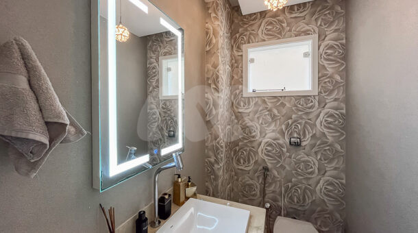 Imagem de lavabo com papel de parede de rosas, espelho com led, branca com cuba e lustre em Casa triplex