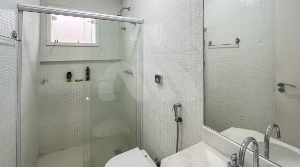 Imagem de banheiro com ladrilhos branco, bancada branca e box com nicho em casa na Barra da tijuca