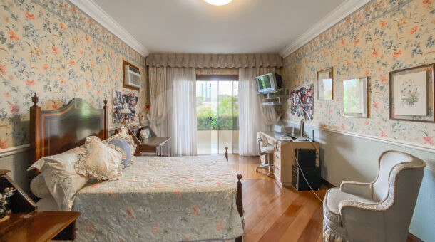 Imagem de quarto com cama de casal, poltrona acolchoada e papel de parede florido em casa duplex a venda na Barra