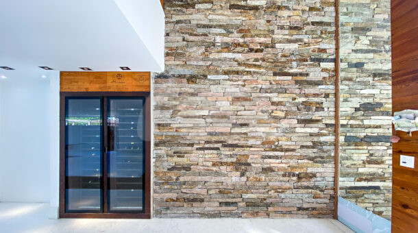 Imagem de hall de entrada com pe direito duplo e parede em tijolos de pedra e adega
