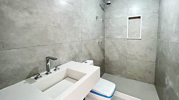 Imagem de banheiro com porcelanato cinza, bancada branca e chuveiro em casa moderna