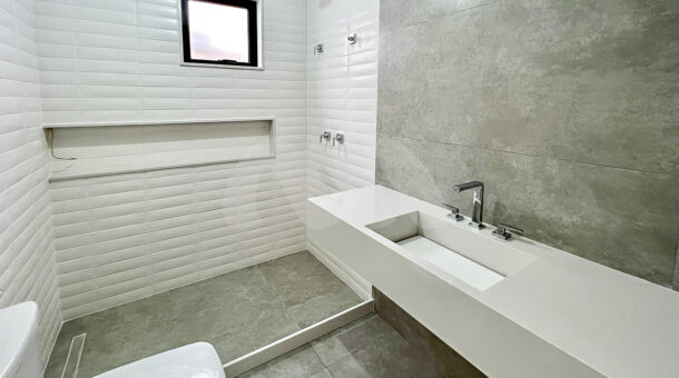 Imagem de banheiro com bancada em pedra branca, pia esculpida, box com nicho e vaso em casa linda contemporanea a venda