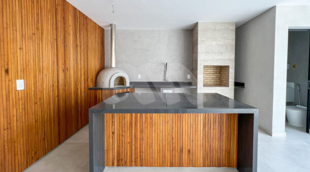 Imagem da área gourmet com painel de madeira, churrasqueira e forno de pizza da casa à venda em condomínio de alto padrão.