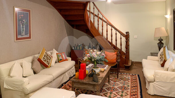 Imagem de sala de estar com sofás brancos, mesa de centro de madeira e escada em madeira