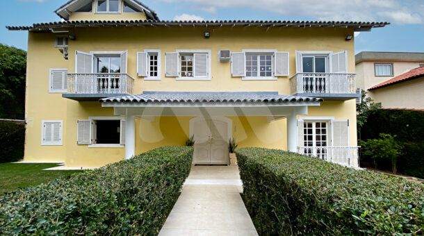 Imagem da fachada amarela e com paisagismo da casa à venda em condomínio de alto padrão.