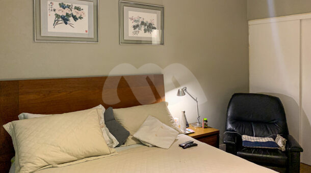 Imagem de quarto com cama de casal, mesa de cabeceira e poltrona em casa duplex a venda