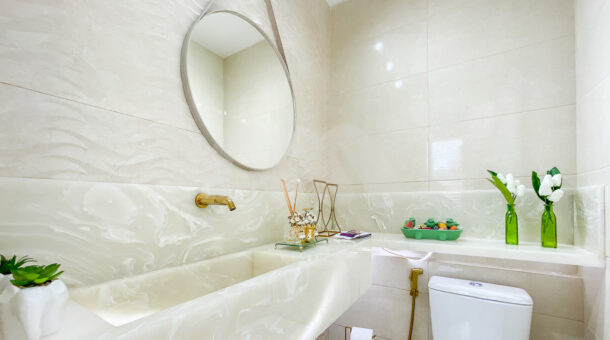 Imagem de lavabo em tom bege claro, com bancada em pedra com iluminaçaõ embutida, e metais em dourado da casa linda contemporanea
