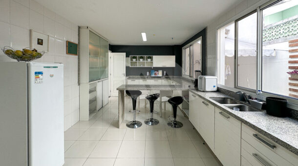 Imagem da cozinha com grande bancada da casa Triplex em estilo tradicional á venda na Barra da Tijuca. Imobiliária de luxo RJ