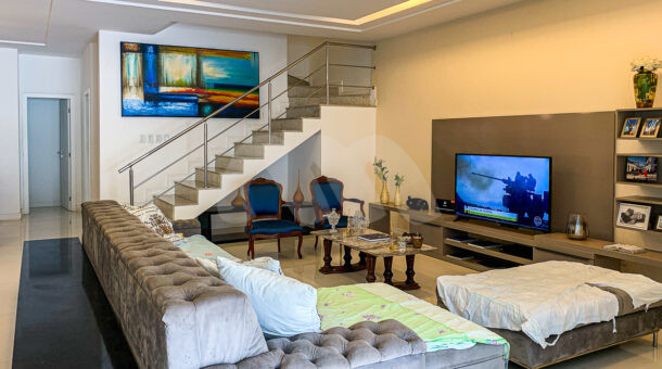 Imagem de sala de estar com sofá cinza, poltronas azul e painel de tv em linda casa à venda no Rio Mar