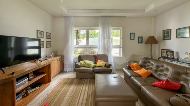 Imagem de sala de tv com sofás em couro marrom, banco e rack de madeira com tv