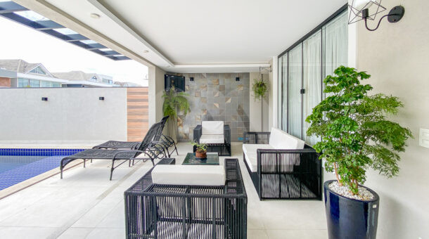 Imagem de varanda externa com moveis preto e branco, e integração a piscina da Casa Triplex contemporânea no Art Life