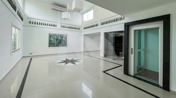 Imagem lateral com vista da ampla sala e elevador do imóvel de luxo à venda.