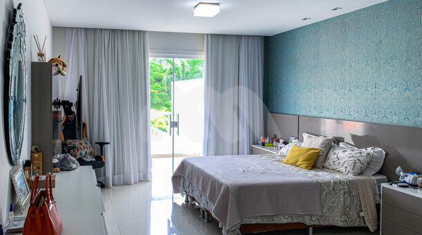 Imagem de quarto com cama de casal, cabeceira e mesa de cabeceira em móvel planejado e papel de parede azul da casa a venda na Barra da Tijuca RJ