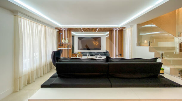 Imagem de sala ampla com painel em ripado de madeira, sofá retratil e tv em Bela Casa triplex