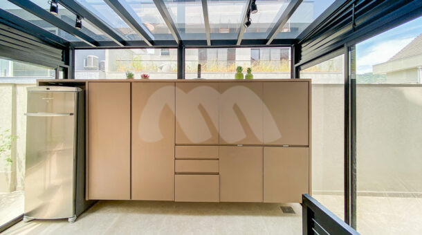 Imagem de espaço coberto de vidro com armarios planejados e geladeira de apoio em casa triplex a venda na Muller Imoveis