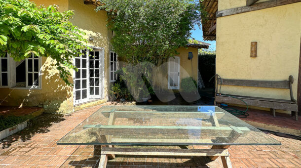 Imagem da área externa com mesa e paisagismo da casa linear à venda na Muller Imóveis de luxo RJ - Recreio
