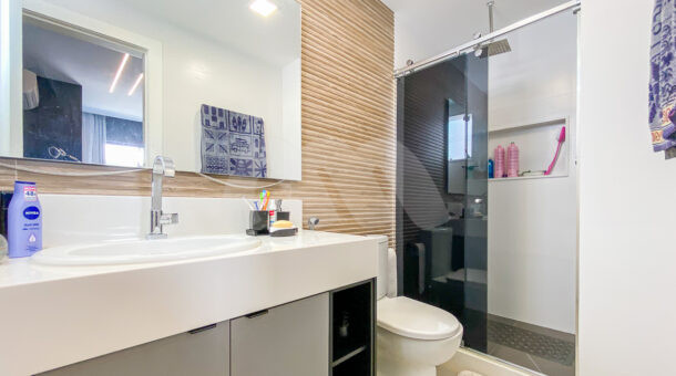 Imagem de banheiro com parede em painel ripado, box com nicho e bancada com cuba e armário planejado com nicho