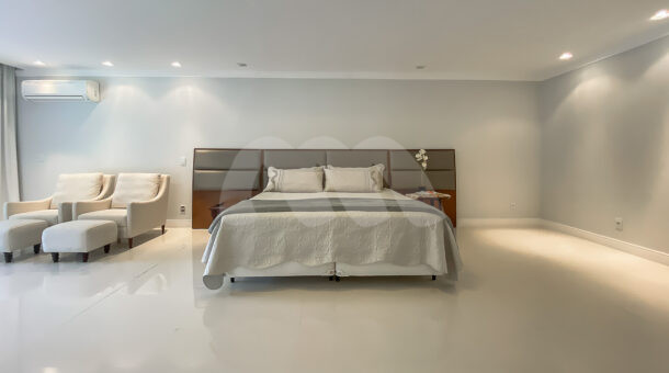 Imagem de suite com cama de casal e cabeceira com poltronas e puff