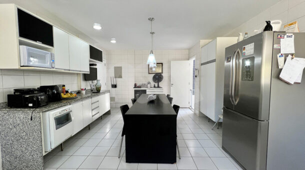 Imagem de cozinha planejada com mesa e armários da casa duplex à venda no condomínio quintas do rio na barra da tijuca